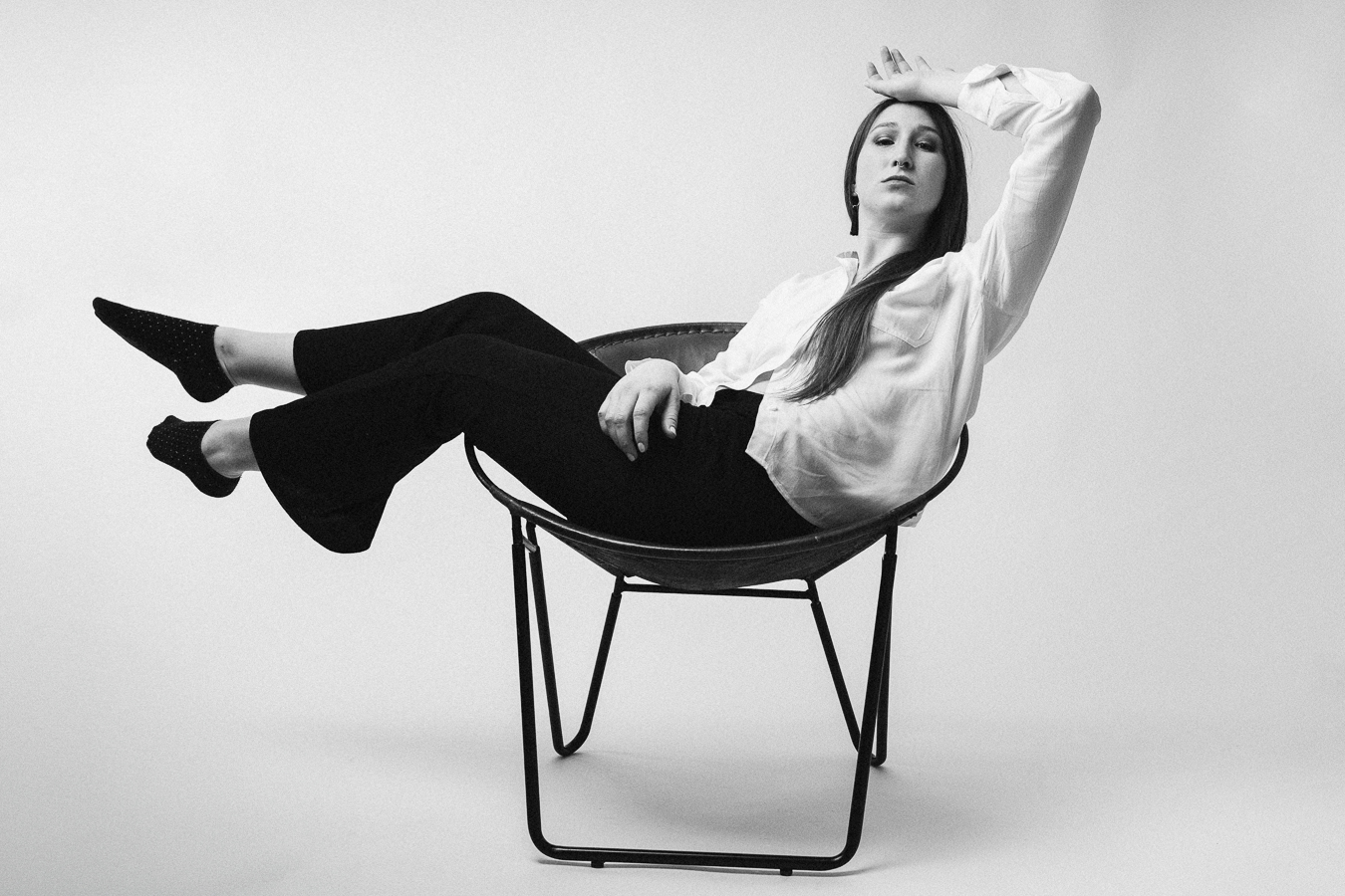 A woman seated in a chair, elegantly crossing her legs, exuding a sense of poise and relaxation.