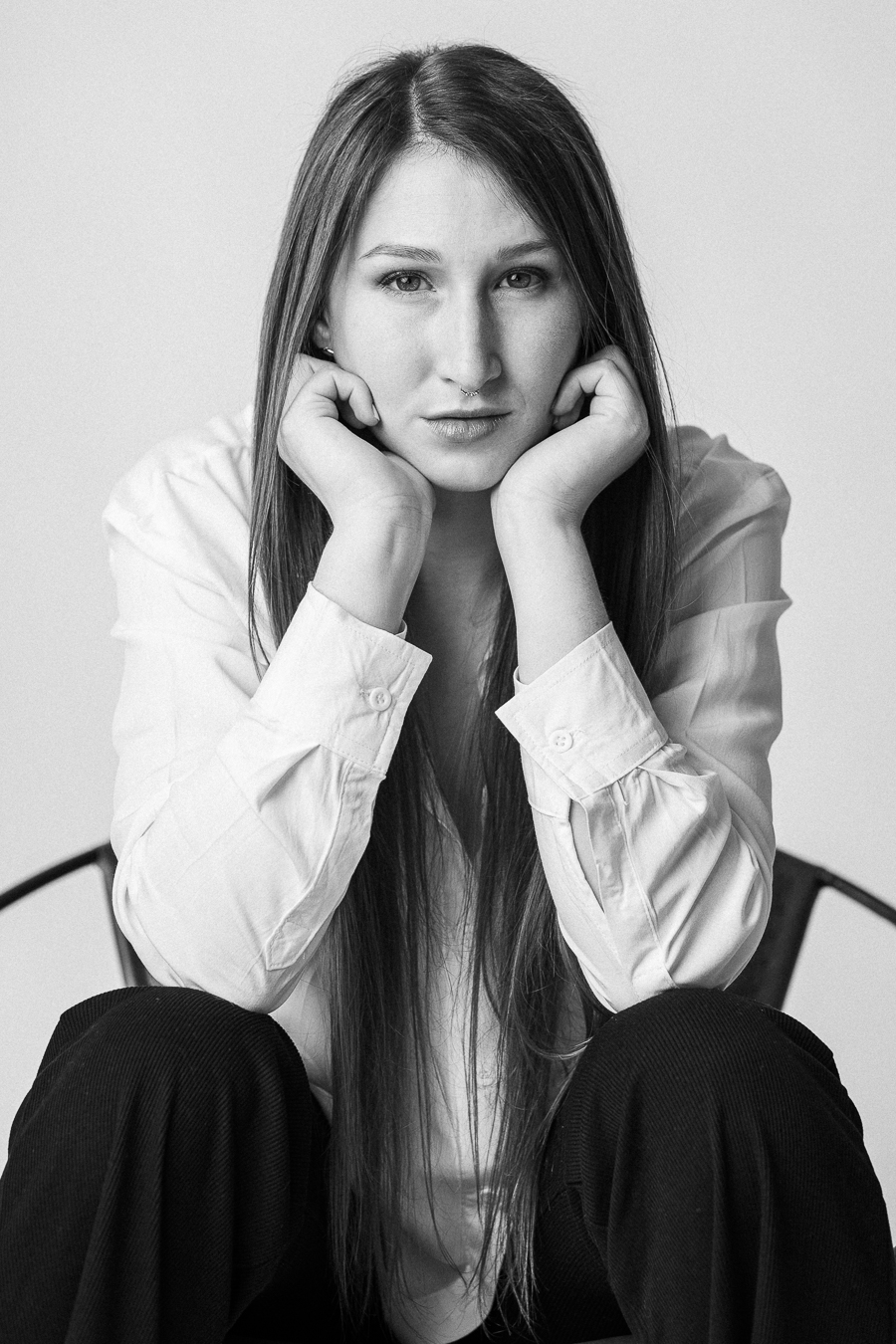 A woman sits thoughtfully on a chair, resting her chin on her hands, reflecting in a moment of contemplation.