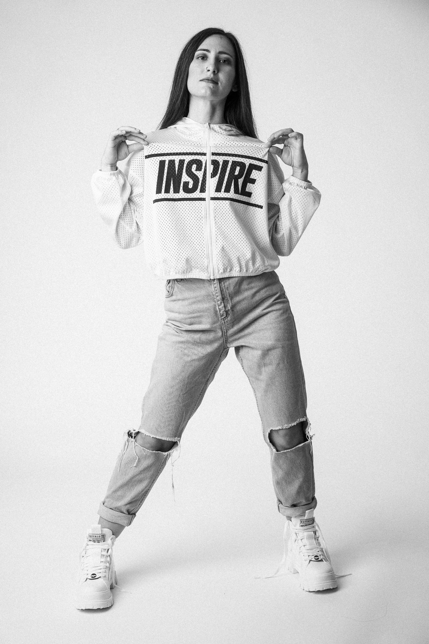 Black and white image of a person wearing a stylish 'Inspire' hoodie, ripped jeans, and white sneakers, striking a confident pose. Fashion photography, modern street style inspiration.