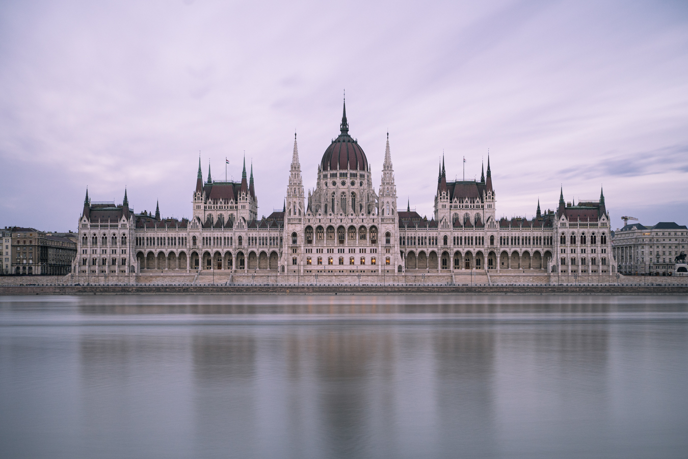 Majestic view of Budapest's Parliament building, reflecting on the Danube River under a cloudy sky.