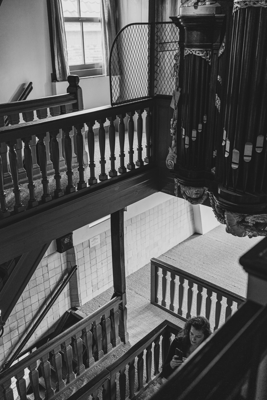 A black and white image of a staircase featuring ornate wooden railings, large windows, and a vintage interior design ambiance.