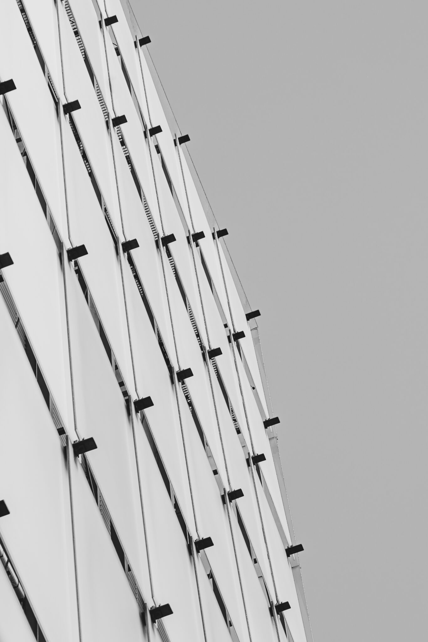 Abstract view of a modern building facade, featuring angular white panels and dark metal brackets against a grey sky.