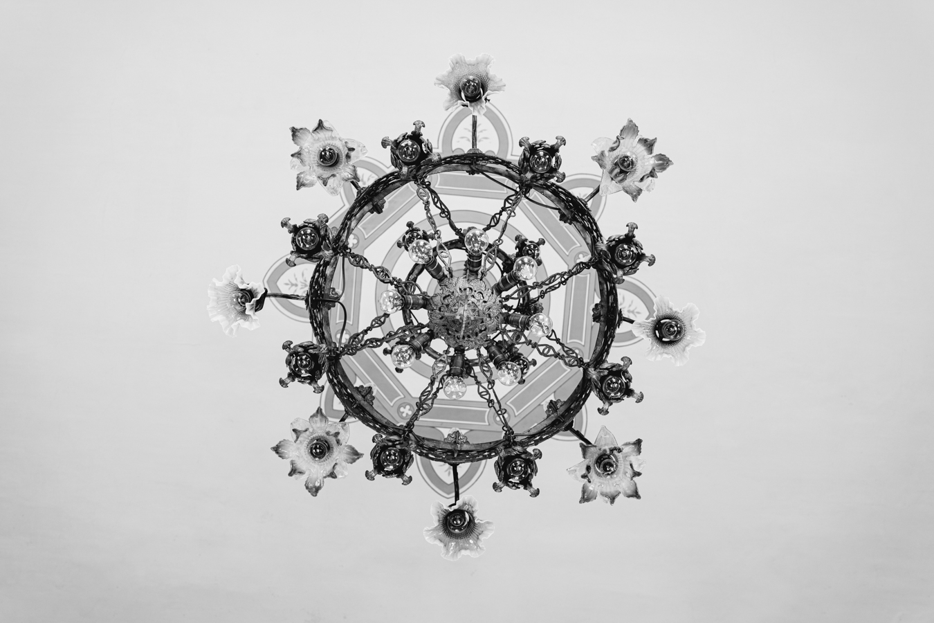 A black and white overhead view of an ornate chandelier with floral details and circular design elements on a plain background.
