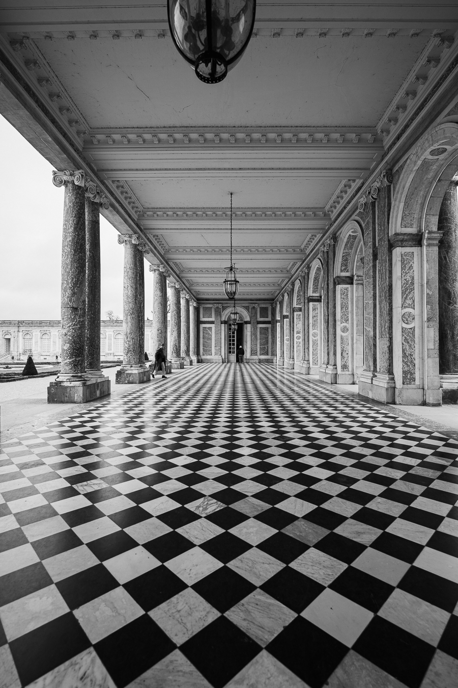 Elegant corridor with checkered floor, columns, and hanging lanterns.