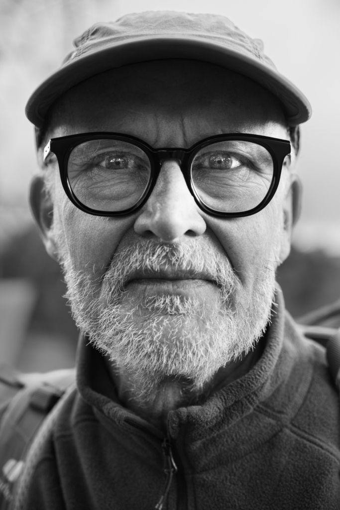Portrait of a man wearing round glasses and a flat cap.