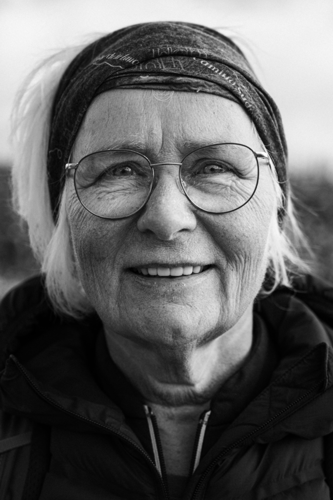 Portrait of an older woman wearing a hat and scarf, smiling.