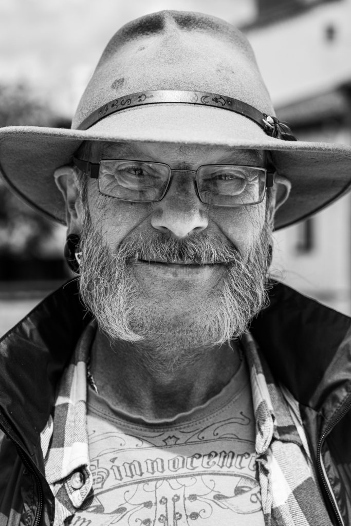Portrait of a smiling older man wearing glasses and a hat.