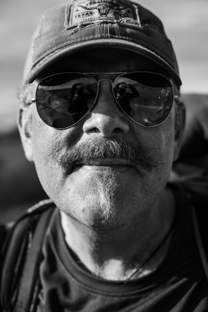 Portrait of a man wearing sunglasses and a hat, smiling slightly.