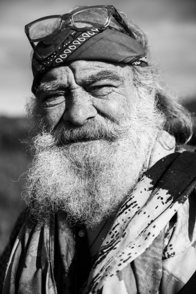 Portrait of an older bearded man wearing a hat and scarf.