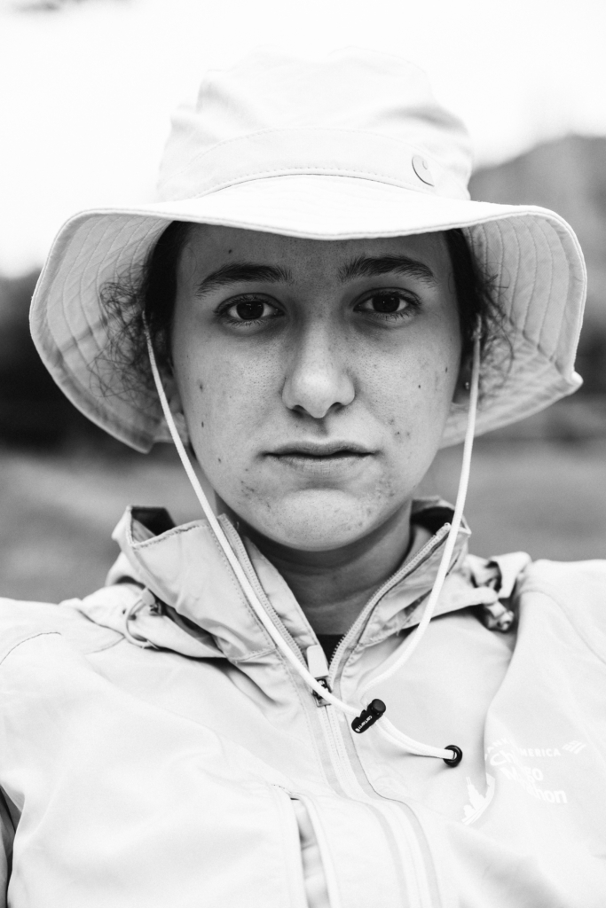 Portrait of a person wearing a wide-brimmed hat and jacket, looking directly at the camera.