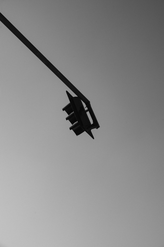 A traffic light hanging against the sky, photographed in black and white.